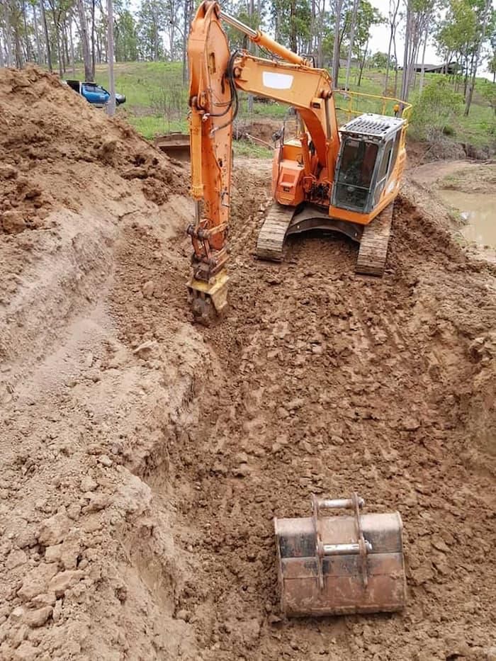 A Large Orange Excavator is Digging a Hole in the Dirt — B E Laser Levelling QLD in Rockhampton, QLD