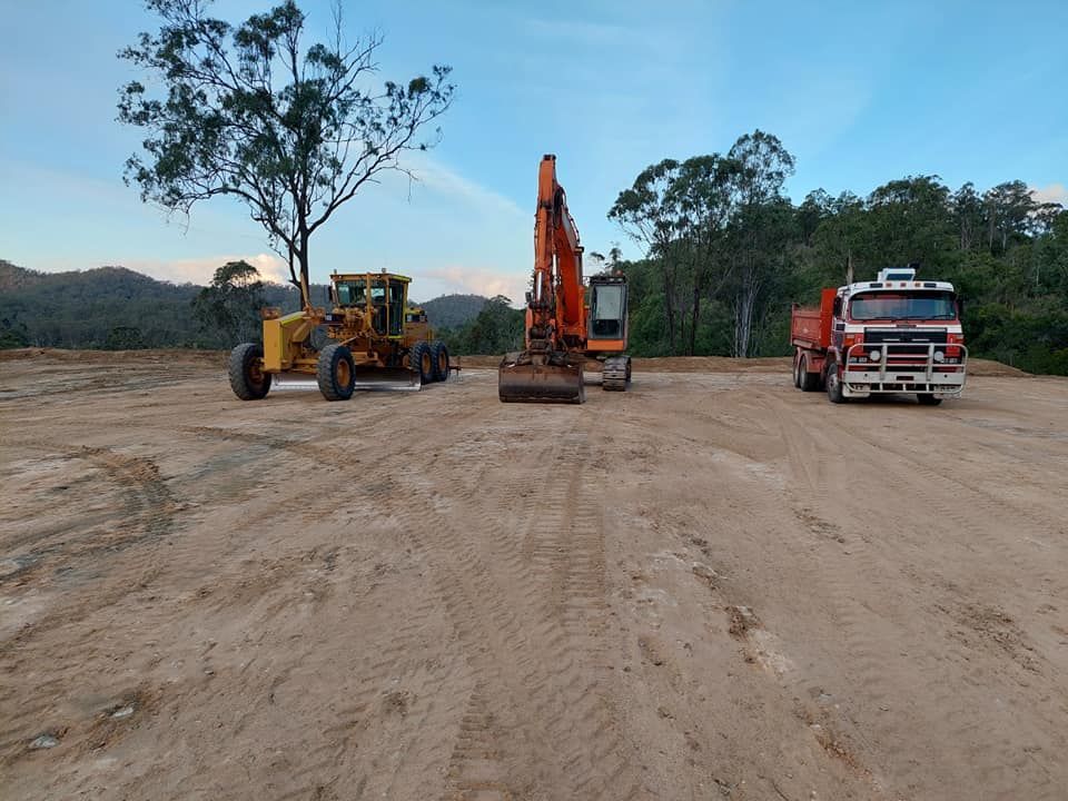 A red truck is parked next to a yellow excavator — B E Laser Levelling QLD in Bucca, QLD