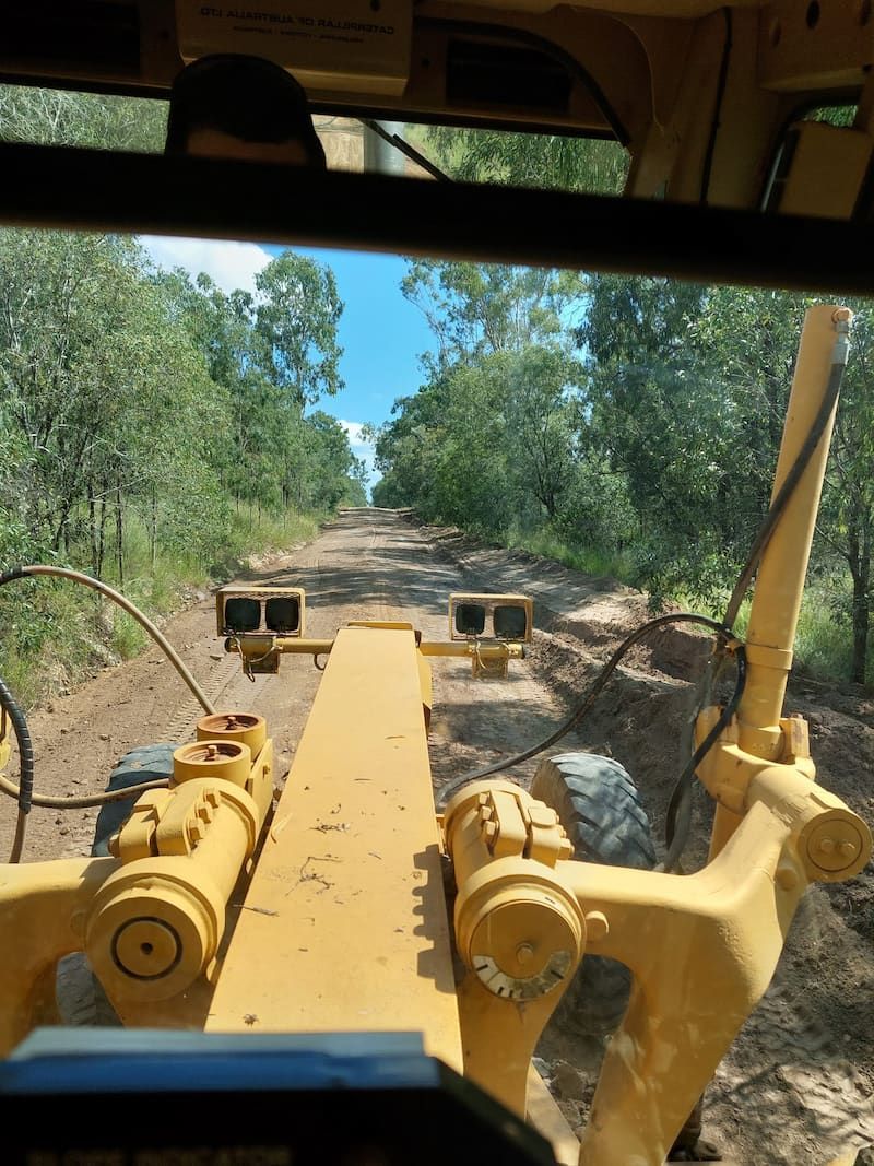 A Yellow Bulldozer is Driving Down a Dirt Road — B E Laser Levelling QLD in Bucca, QLD