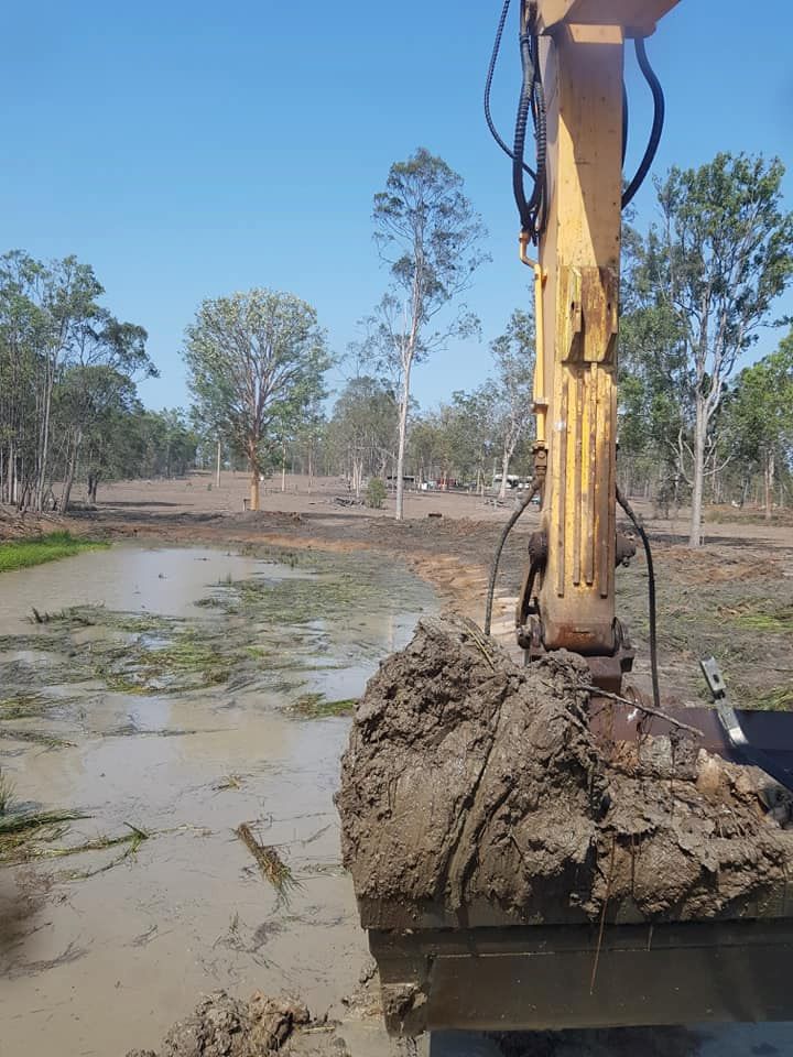 A Yellow Excavator is Digging a Hole in the Mud — B E Laser Levelling QLD in Childers, QLD