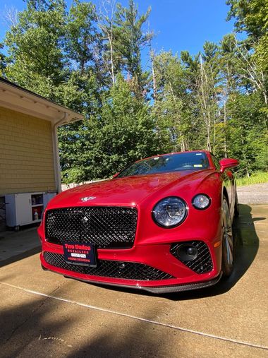 Red sports car parked beside a black truck on a wet road near trees