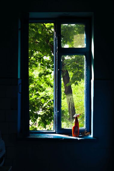 Dim room with open window, green trees outside, and a small red bottle on the sill.
