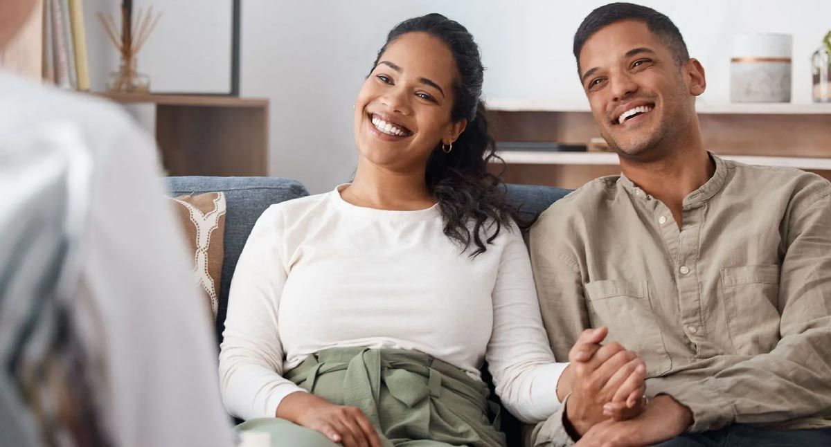 A man and a woman are sitting on a couch holding hands and smiling.