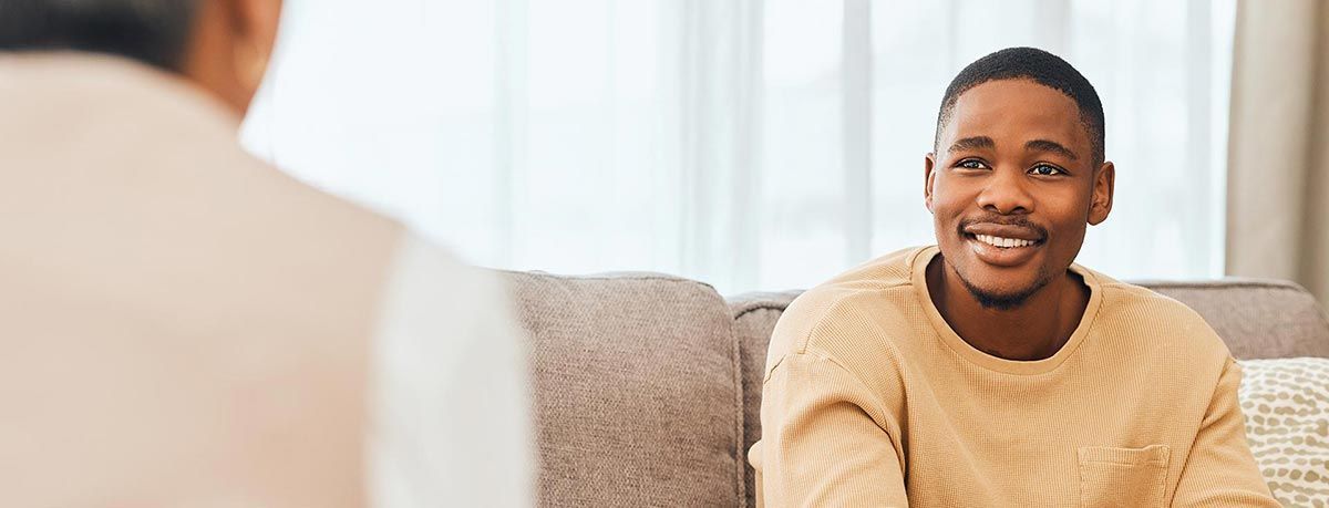 A man is sitting on a couch talking to another man.