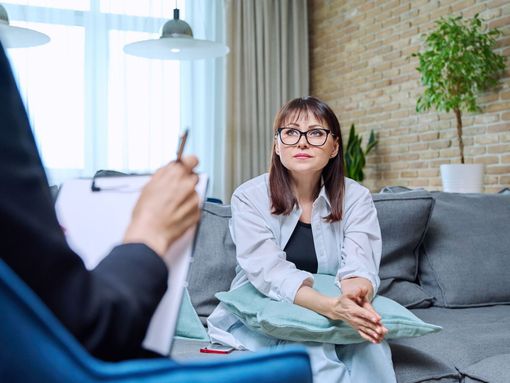 A woman wearing headphones is smiling while sitting on a couch.