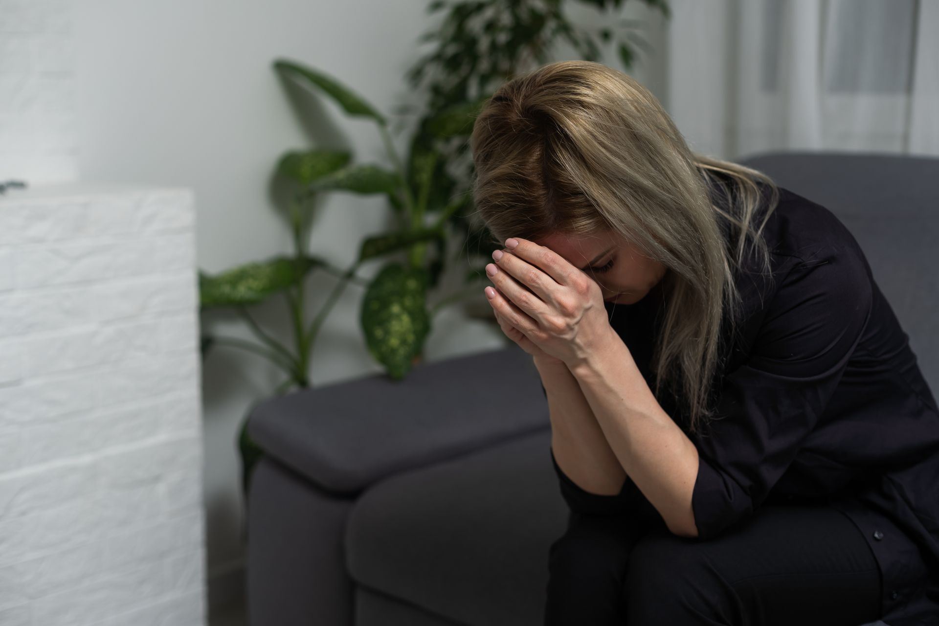 A woman is sitting on a couch with her head in her hands.