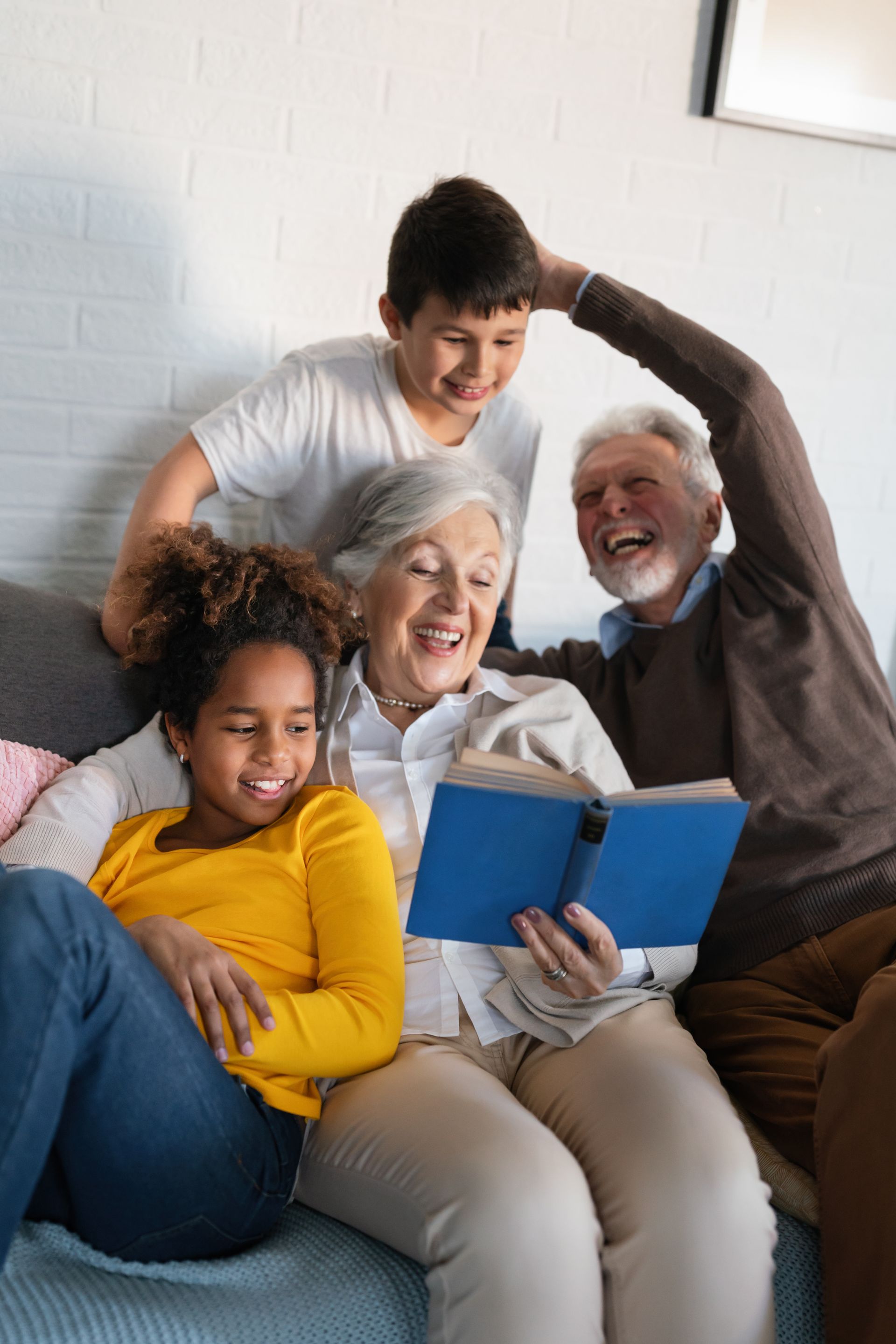 Family laughing while reading a book on a couch.