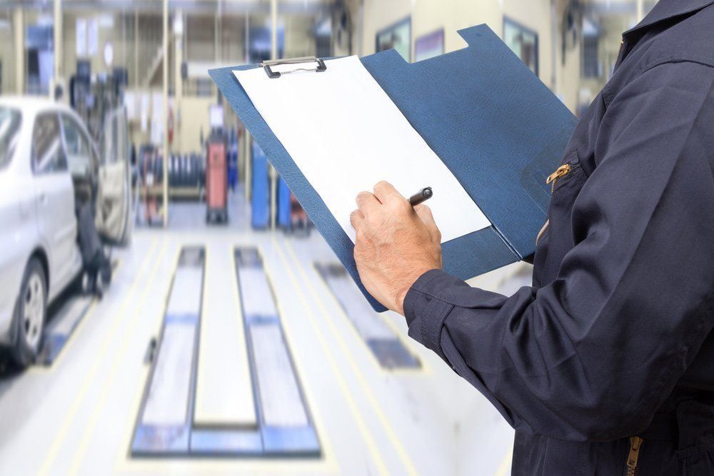 A Mechanic Is Writing On A Clipboard In A Garage — Dancers Car Care In Ballina, NSW
