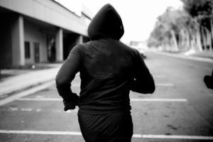 A man in a black hoodie is running down a street