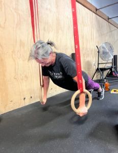 A woman is doing push ups on gymnastic rings in a gym.