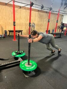 A woman is pushing a sled in a gym.