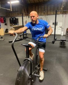 A man in a blue shirt is riding an exercise bike in a gym.