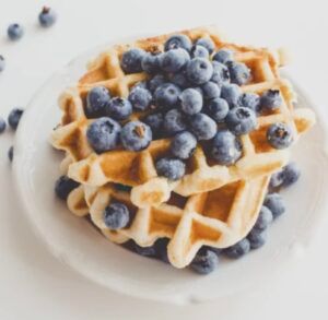 Two waffles stacked on top of each other with blueberries on a white plate.