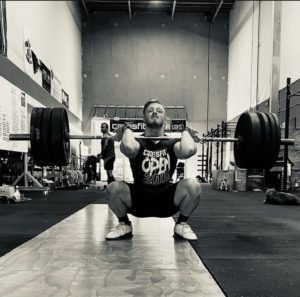 A man is squatting down while holding a barbell in a gym.