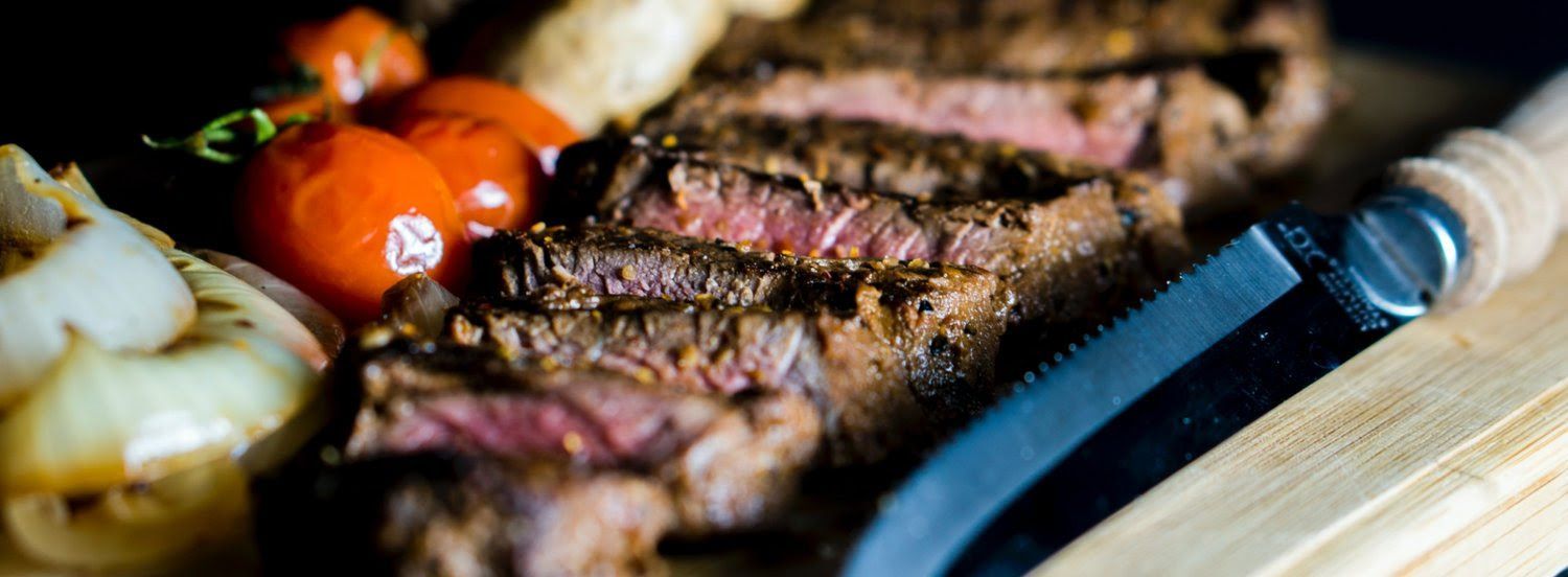 A close up of a steak on a wooden cutting board with tomatoes and onions.