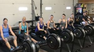 A group of people are sitting on rowing machines in a gym.