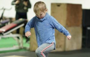 A little girl is standing on one leg in a gym.