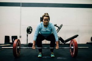 A woman is squatting down to lift a barbell in a gym.