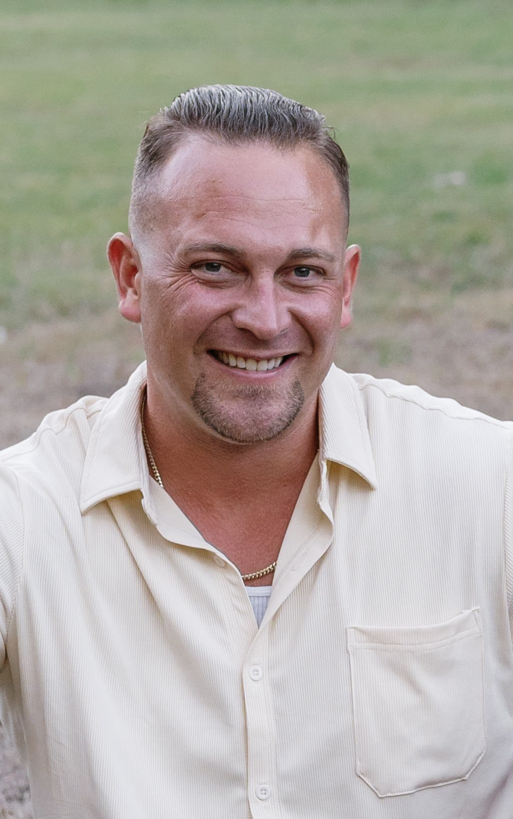Woman in safety vest and hard hat smiles, arms crossed against a gray background.