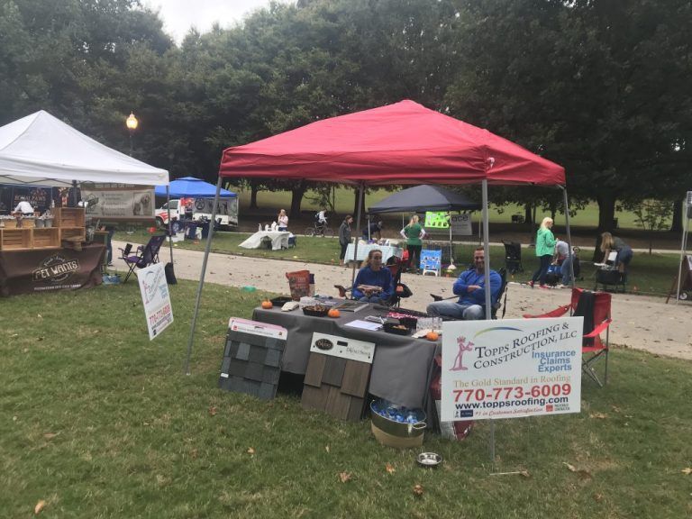 A construction company booth under a red tent at an outdoor event; two men sit at the table.