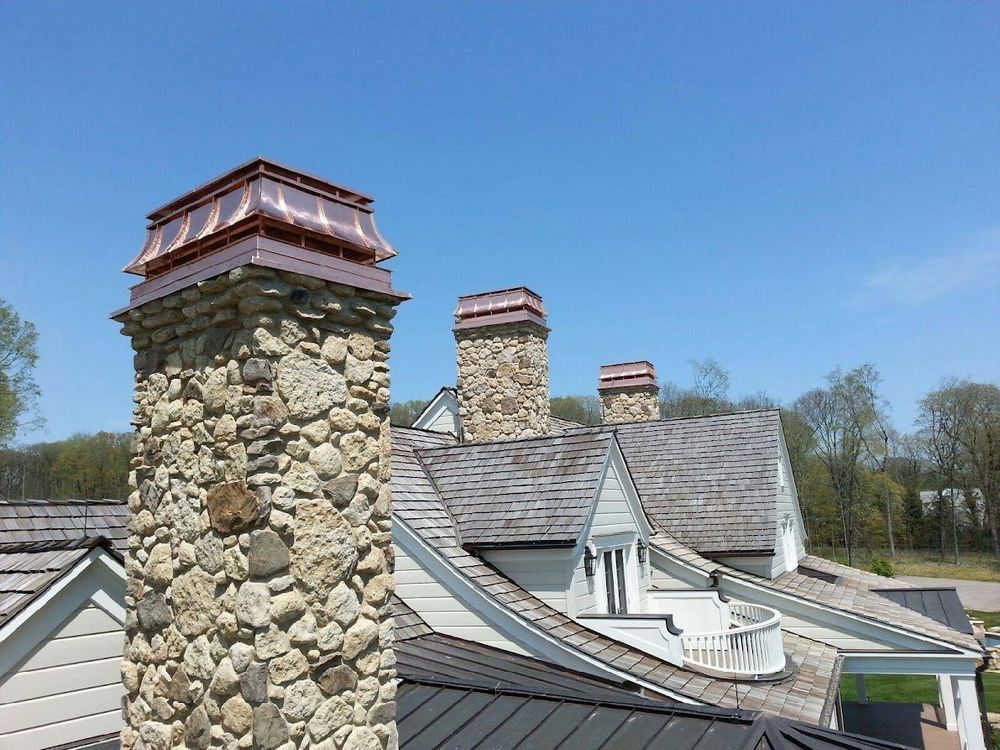 Stone chimneys with copper tops on a wood shingle roof against a blue sky.