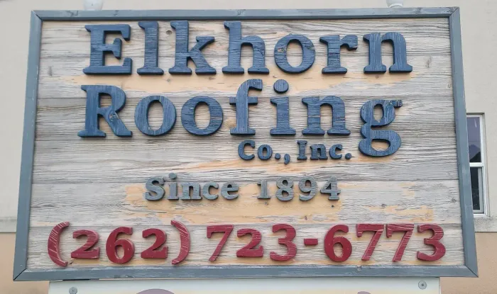 Sign for Elkhorn Roofing Co., Inc. on a weathered wooden background with phone number.