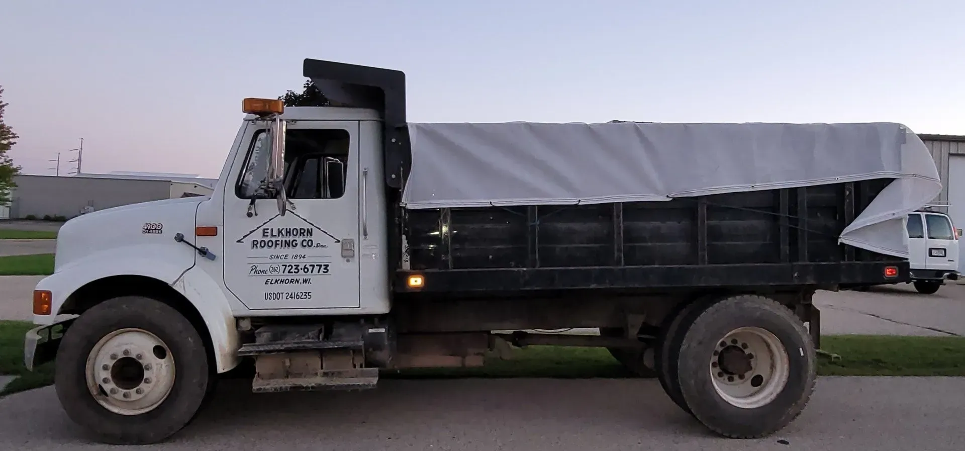 White dump truck with black bed and tarp on side of road.