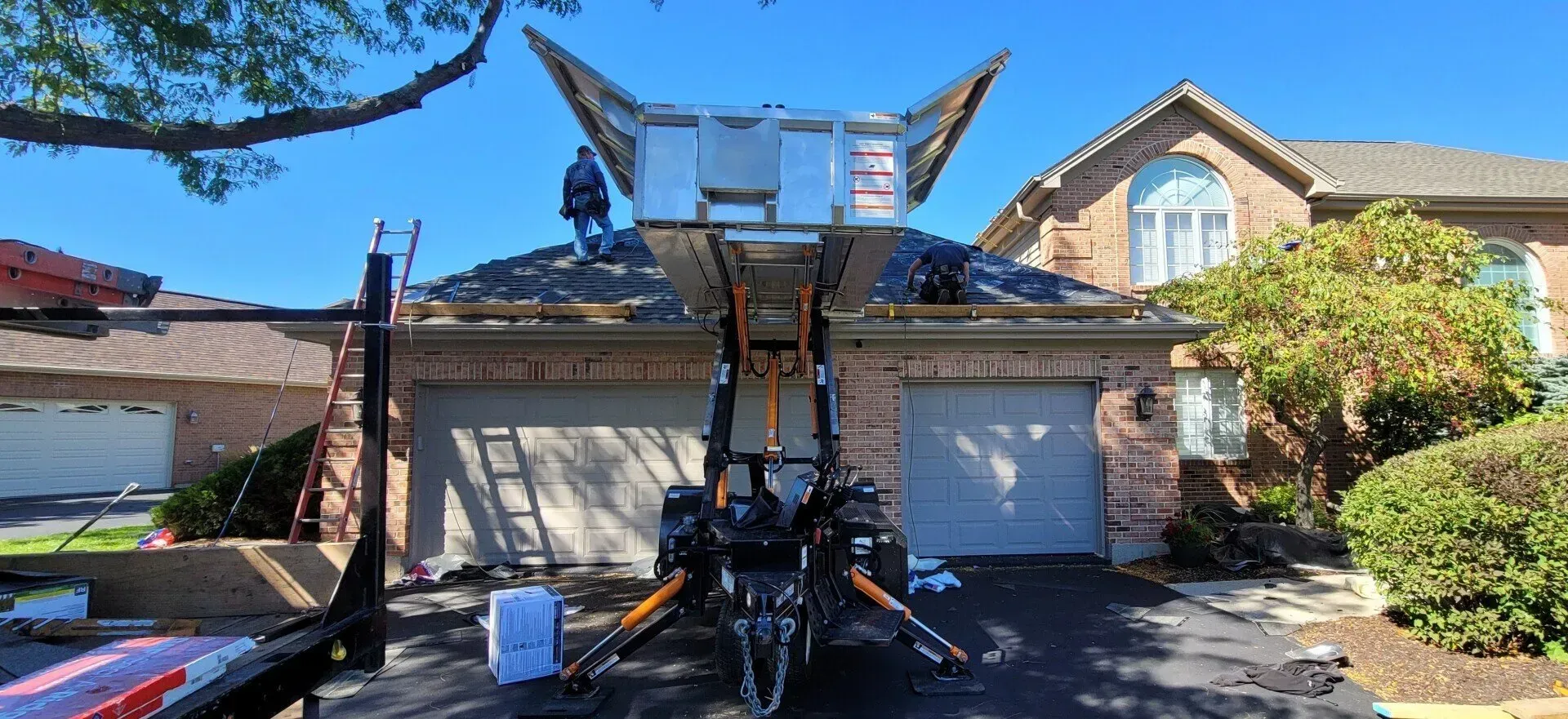 A roofer on a house roof is working with a lift. Sunlight and blue sky are in the background. A roofer on a house roof is working with a lift. Sunlight and blue sky are in the background.