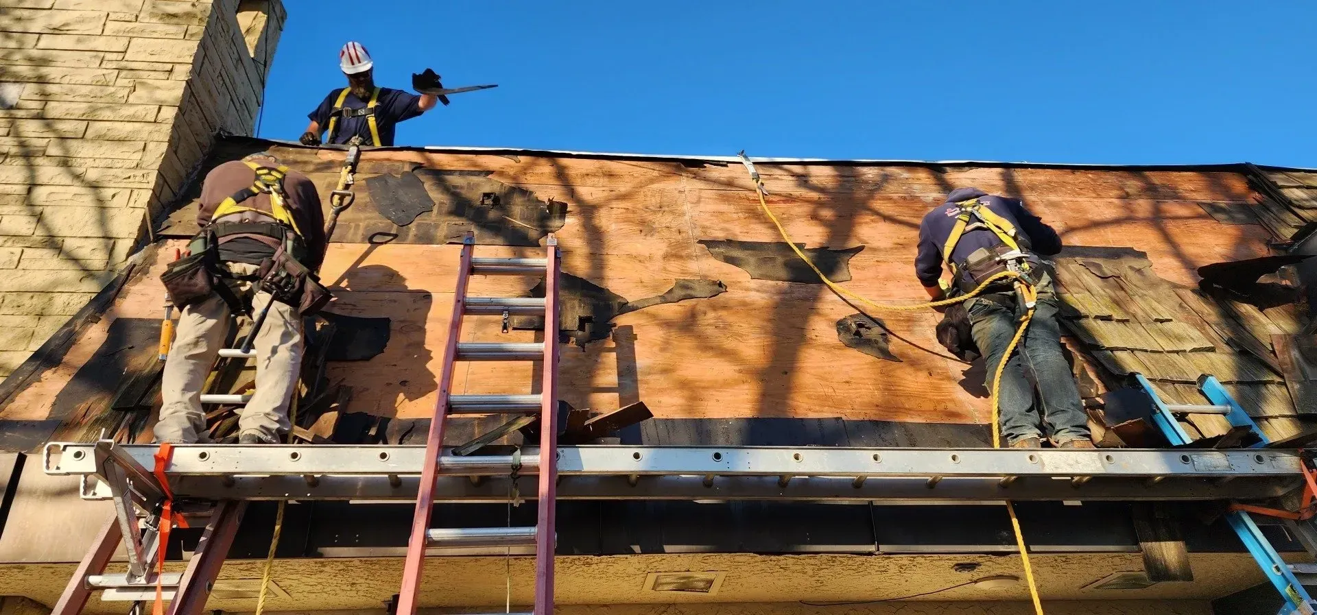Three workers on a roof, securing ropes, two on scaffolding, one near a chimney. Clear blue sky. Three workers on a roof, securing ropes, two on scaffolding, one near a chimney. Clear blue sky.