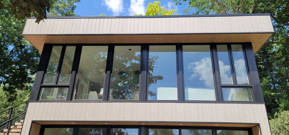 Modern building with large windows reflecting blue sky and trees.