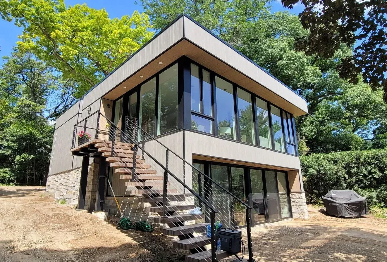 Modern two-story house with glass walls, exterior stairs, and surrounded by trees.