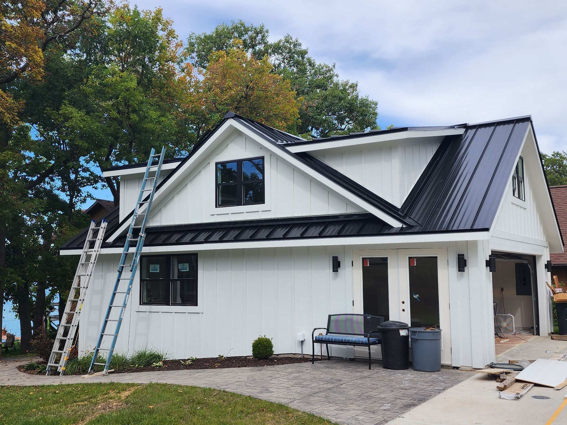 White house with black roof and trim. A-frame style. A ladder is propped against the side.