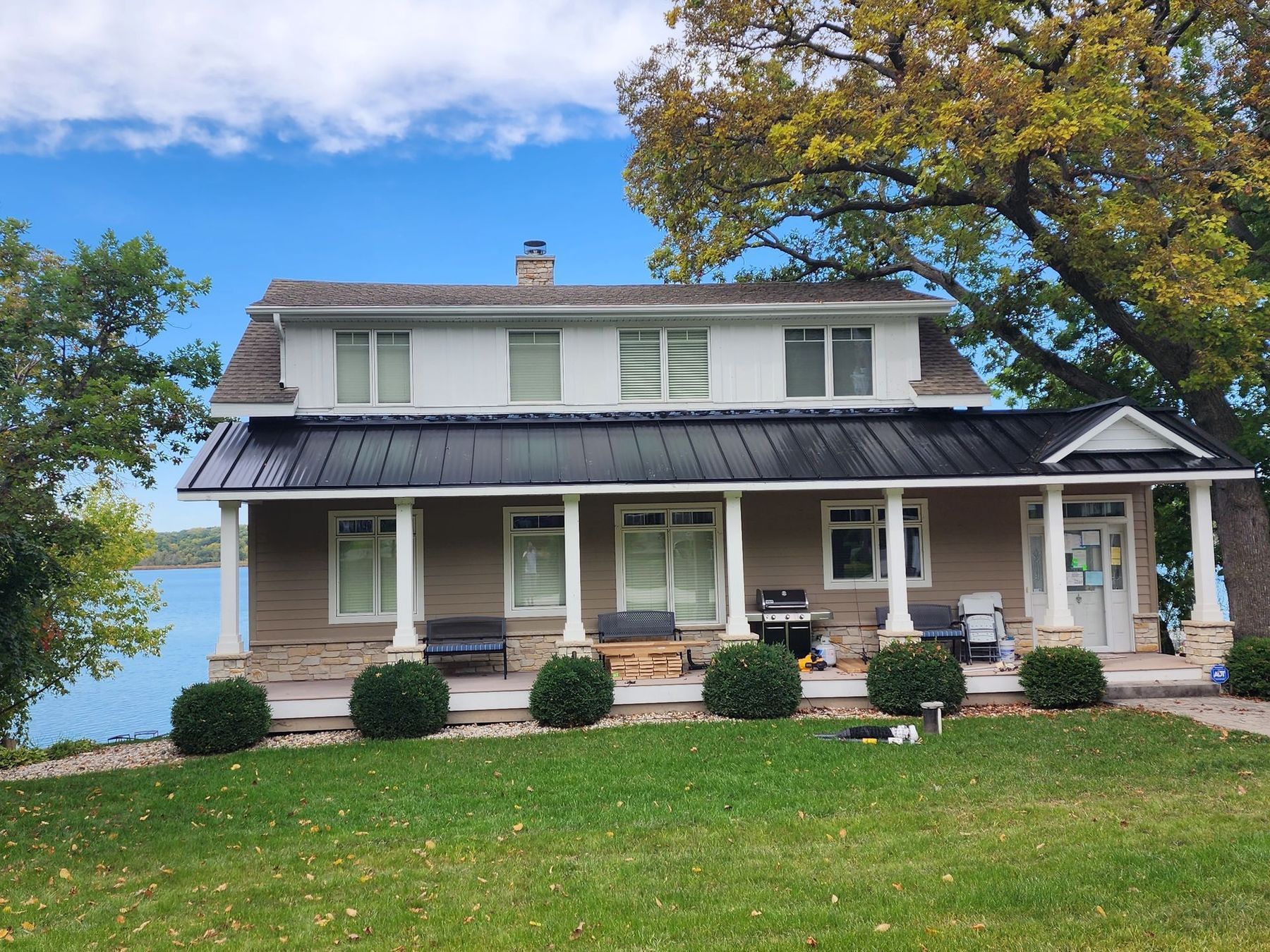 Two-story house with black roof and white pillars on a lake, green lawn.