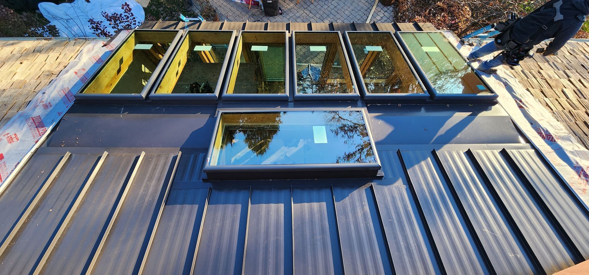 A roof with multiple skylights installed. A person with a gloved hand reaches.
