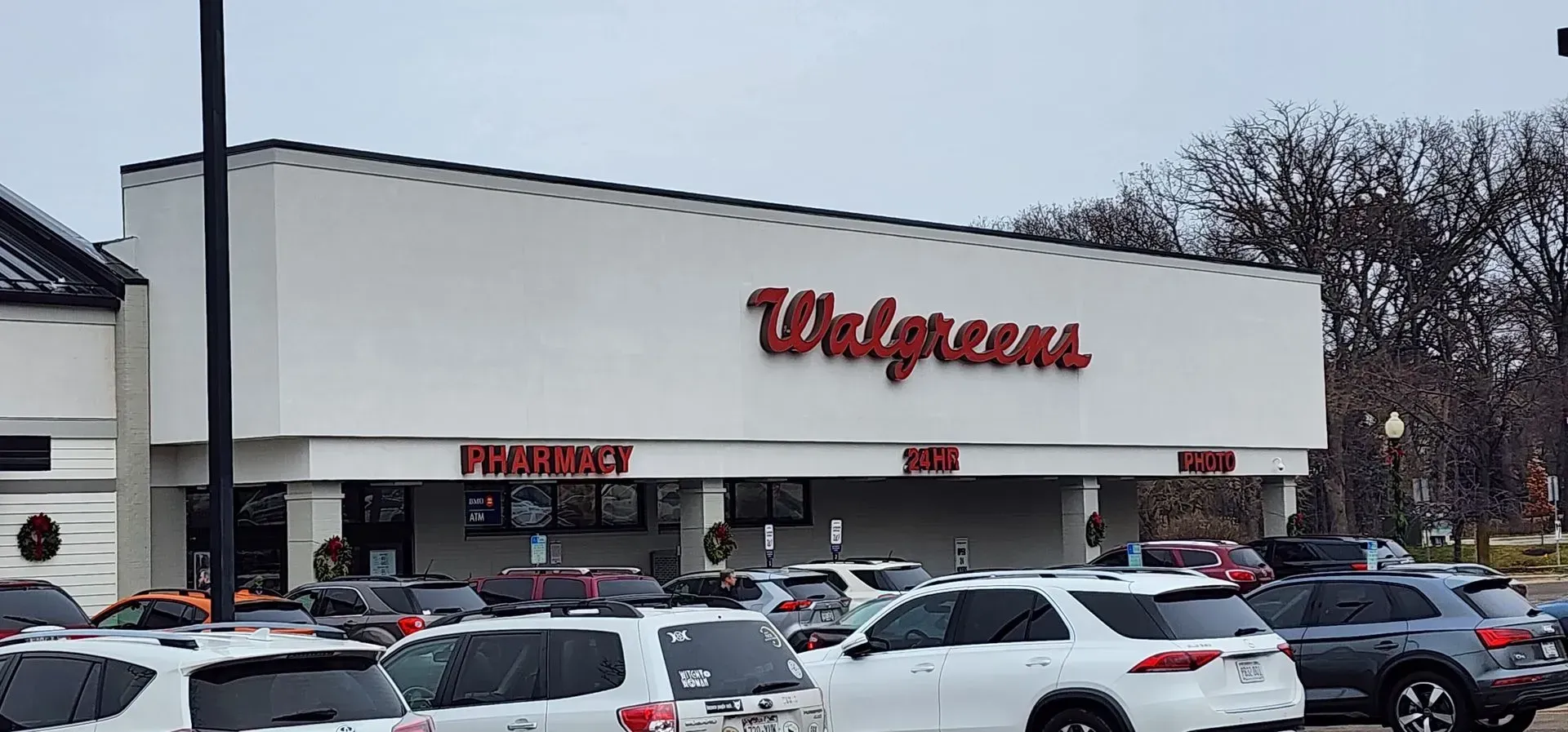 Exterior of a Walgreens store with the red logo on a white facade. The pharmacy, and shop is visible, and the parking lot has vehicles. The pharmacy, and shop is visible, and the parking lot has vehicles.