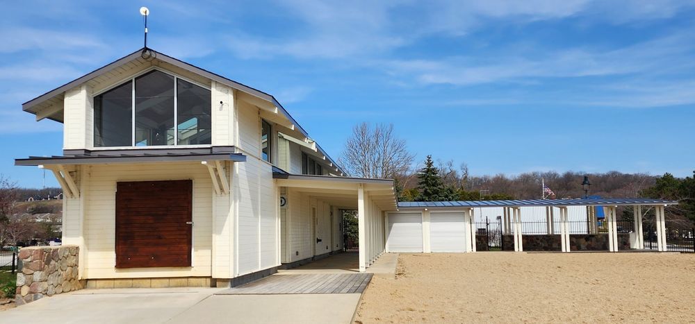 Exterior view of a light-colored building with large windows and a covered walkway, against a blue sky.