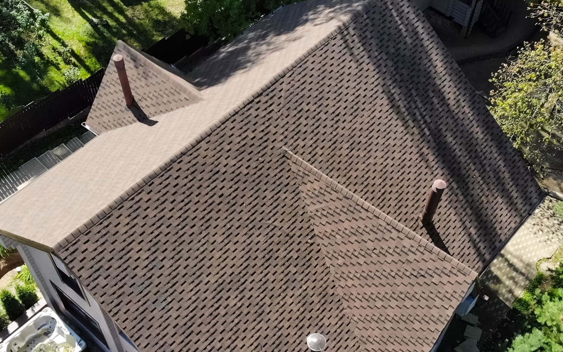 Brown shingled roof of a house with chimneys, viewed from above.