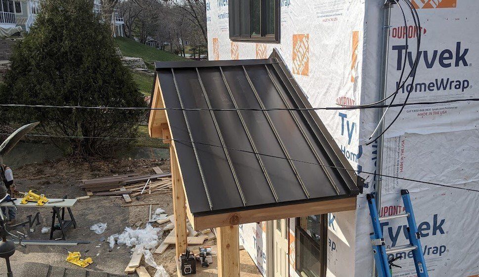 Metal awning being installed over a window, on a building under construction, with wooden supports.