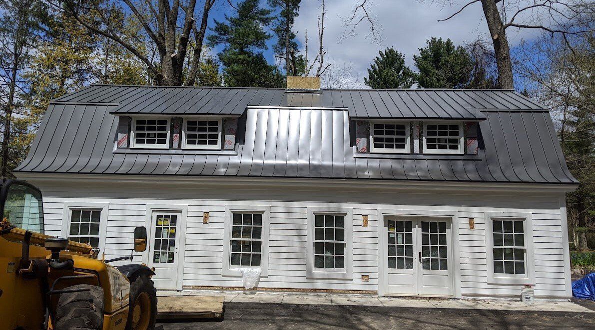 White house with gray roof, metal roofing details, windows, and construction equipment.