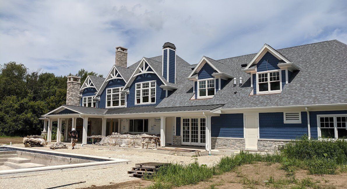 Large blue house with a gray roof and stone accents, under construction near a pool.
