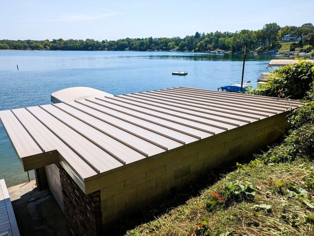 Dock on a lake with light-colored, horizontal planks. Building sits in the water with trees on the horizon.