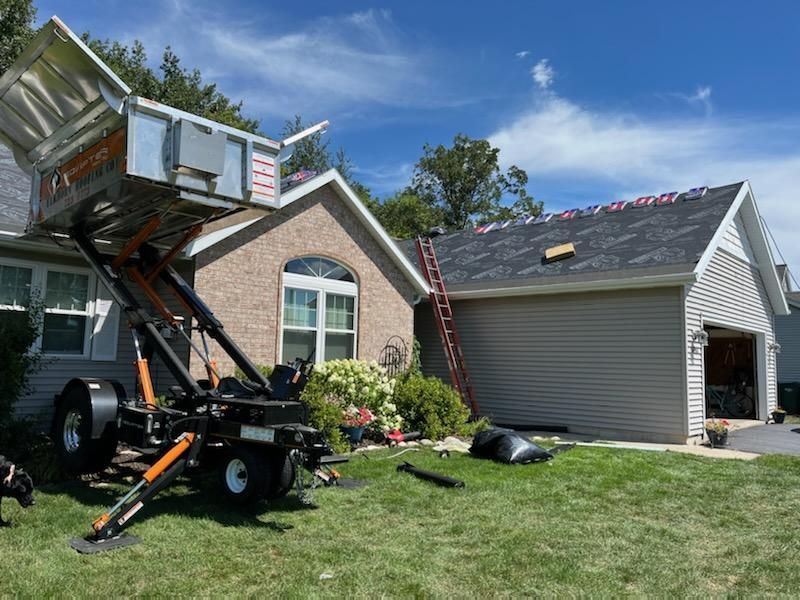 A house with a roof being worked on, a lift used to move construction materials is set up on the lawn.