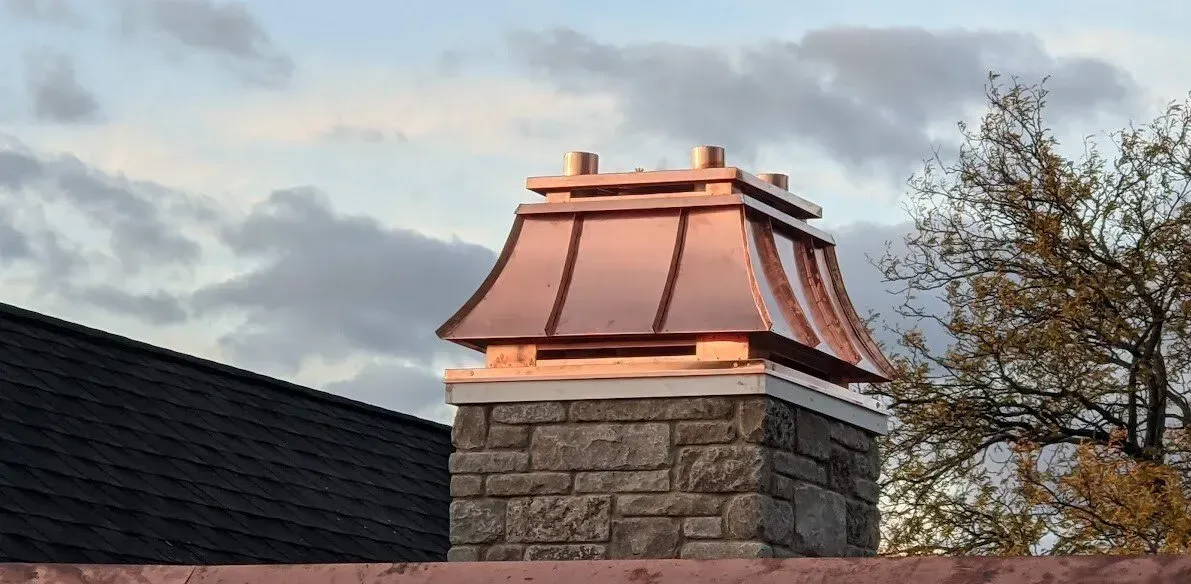 Stone chimney with copper roof cap against a cloudy sky.