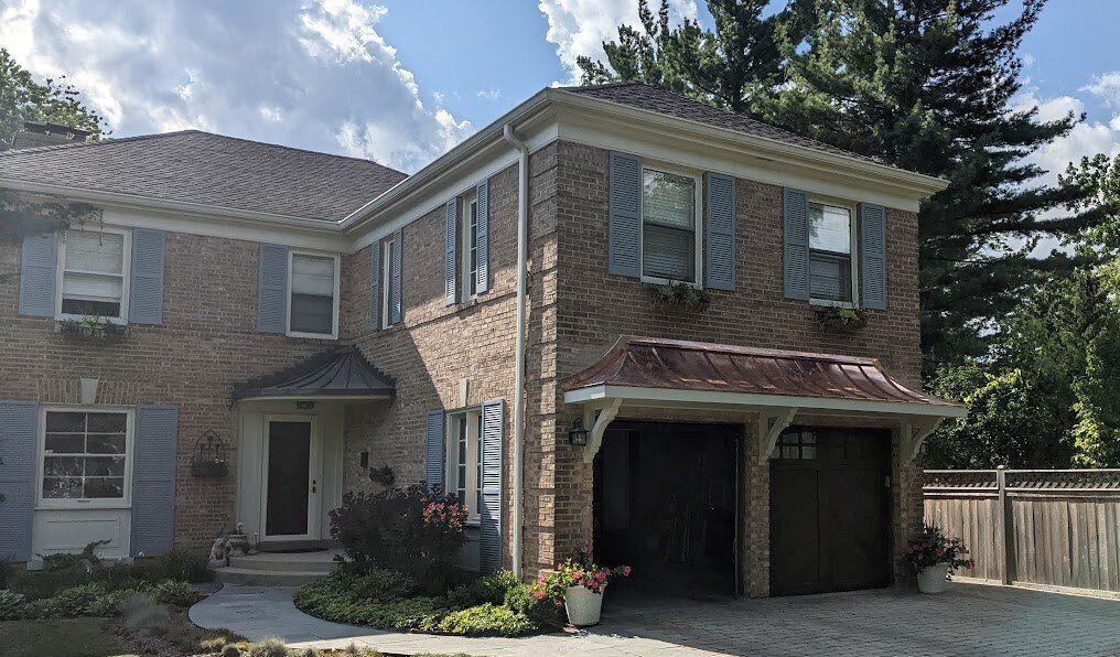 Two-story brick house with blue shutters, copper-colored garage roof, and a blue front door.