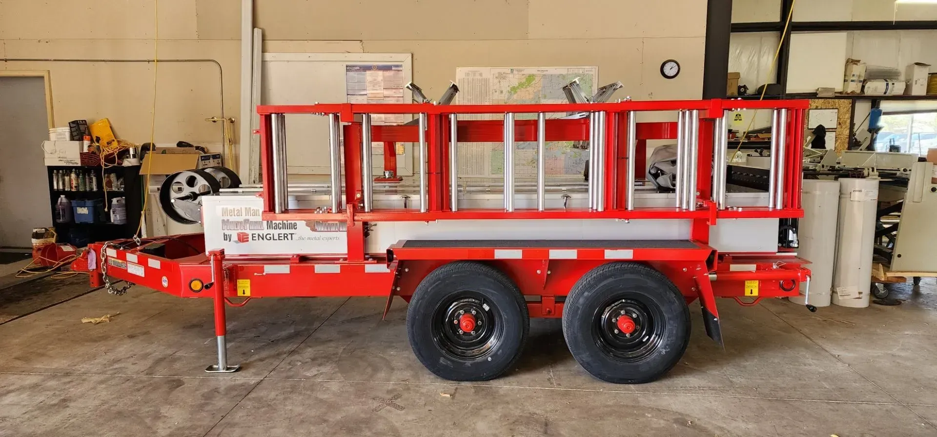 Red and white lift machine on a trailer. Two large black tires, ladder-like lift structure.