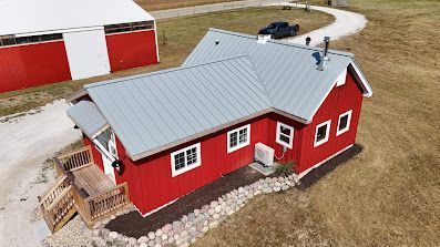 Red farmhouse with gray roof, white trim. Wooden steps lead to porch. Barn in background.