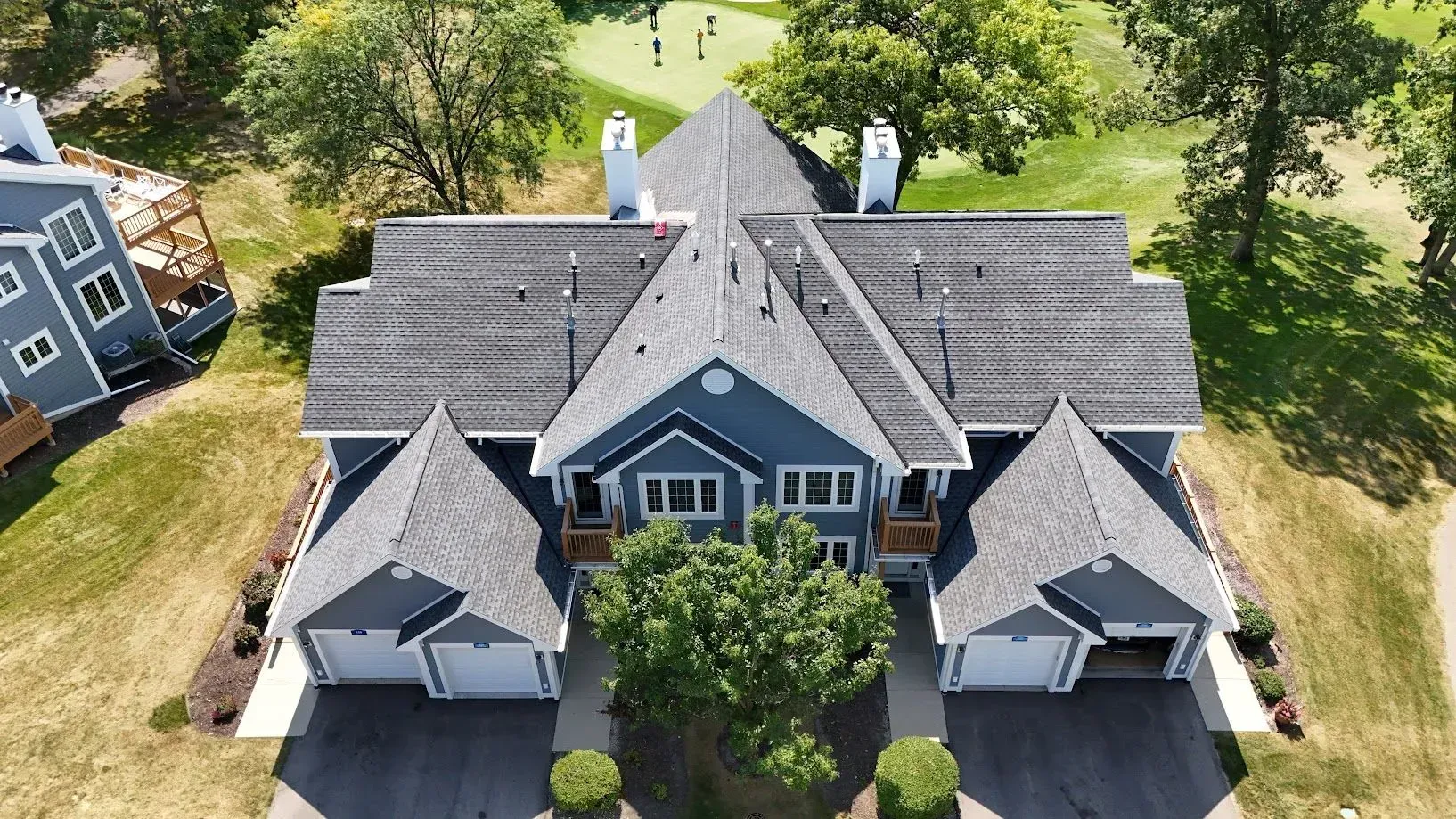 Aerial view of a blue residential building with a gray roof and two garages. A golf course is in the background. Aerial view of a blue residential building with a gray roof and two garages. A golf course is in the background.