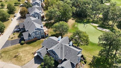 Houses with grey roofs next to a golf course with green grass and trees.