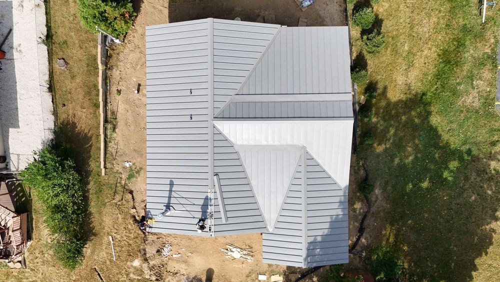 Overhead view of a house with a gray metal roof, surrounded by grass and dirt.