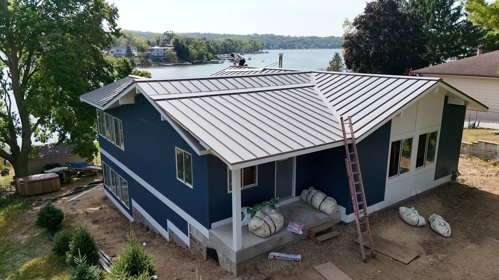 Blue house with metal roof under construction by water.